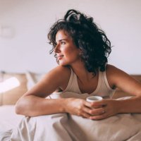 relaxed woman enjoying morning coffee in cozy bedroom - coffee stockfoto's en -beelden