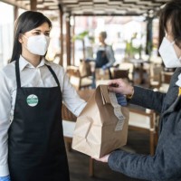 restaurant employee wearing a sticker showing that she has been vaccinated against covid-19, giving a take away food to a customer. - junk food stock pictures, royalty-free photos & images
