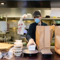 restauranteur wearing mask and gloves packaging food for delivery during covid-19 outbreak - junk food stock pictures, royalty-free photos & images