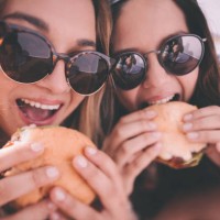 retro style shot of teenage girl best friends eating burgers - junk food stock pictures, royalty-free photos & images