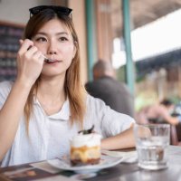süßigkeiten geben ihrem körper energie und sorgen für erfrischung. junge koreanerin, die im café sitzt und ein stück kuchen und kaffee zur entspannung isst, nachdem sie den tempel in bangkok besichtigt hat. essen und trinken 