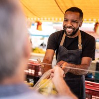 salesman helping the his customer putting the bananas in a plastic bag on a street market - food stock pictures, royalty-free photos & images