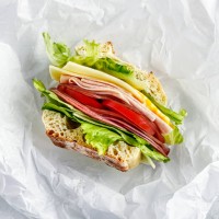 sandwiche with salami, ham, cheese, and tomatoes on parchment paper - junk food stock pictures, royalty-free photos & images