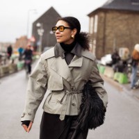 Sara Flaaen Licius wears army green trench crop coat, black leather skirt, orange sunglasses, black leather bag with tassels outside the Munthe...