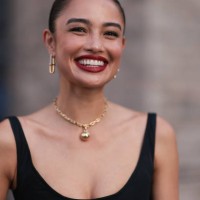 Sara Sampaio is seen wearing yellow-gold earrings a necklace from Tiffany & Co., HardWear Collection and a sleeveless, round-necked, black midi dress...
