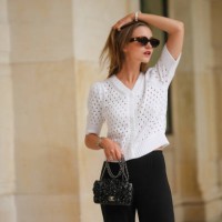 Segolene Hyppolite wears sunglasses, a white wool cardigan / top from Agnes B, a white flower shaped bracelet, a Chanel bag with floral texture /...