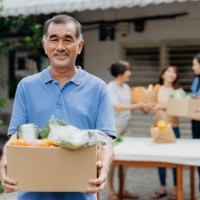 senior asian volunteer holding a box of donated groceries at food bank - food stock pictures, royalty-free photos & images