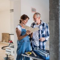 senior couple laying tile floor in new home, using manual cutter. - home decoration stock pictures, royalty-free photos & images