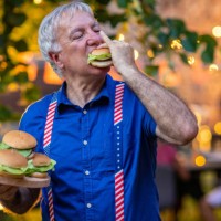 senior man eating a hamburger on celebration of american holiday barbecue party - junk food stock pictures, royalty-free photos & images