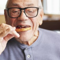 senior man eating toast and jelly jam - food stockfoto's en -beelden