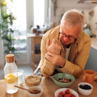 senior man experiencing hand joint pain while having breakfast in the kitchen - food stock pictures, royalty-free photos & images