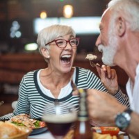 senior woman laughing while feeding her male partner in the restaurant - food stock pictures, royalty-free photos & images