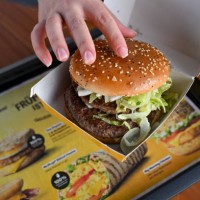 September 2024, Berlin: A woman holds a Burger M in her hands at the opening event of the McDonalds branch in Alboinstraße. The M consists of two...