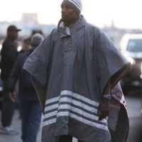 Serge Ibaka wears a wide grey blanket jacket with white stripes, matching grey hat, a white t-shirt and grey suit pants, outside before Thom Browne...