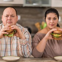 serious overweight couple eating burgers in the kitchen. - junk food stock pictures, royalty-free photos & images