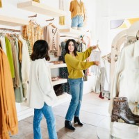 shop owner helping smiling woman choose outfit while shopping in clothing boutique - fashion photos et images de collection