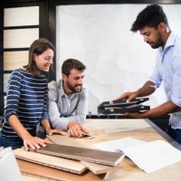 shop seller bringing a small black display case to the table with two customers. a couple of parquet sample planks, a catalog and a smart phone are on the table - home decoration stock pictures, royalty-free photos & images