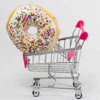 shopping cart with a colorful donut - junk food stockfoto's en -beelden