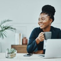 shot of a young businesswoman using a laptop and having coffee in a modern office - coffee stockfoto's en -beelden