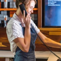 shot of a young woman speaking on the phone behind the counter of a restaurant - junk food stock pictures, royalty-free photos & images