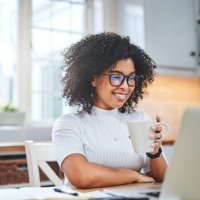 shot of a young woman using a laptop and having coffee while working from - coffee stockfoto's en -beelden