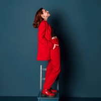 side view of a smiling young woman in a red suit posing standing on a chair in a new clothing collection studio shot indoors - fashion fotografías e imágenes de stock