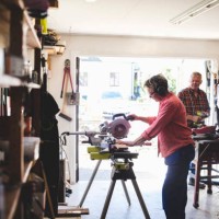 side view of senior woman using circular saw while man holding drill in background - home decoration stock pictures, royalty-free photos & images