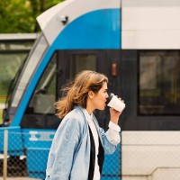 side view of young woman drinking coffee at tram station - junk food stock pictures, royalty-free photos & images