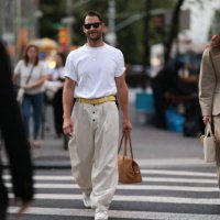 Simon Porte Jacquemus is seen wearing black Wayfarer sunglasses from Ray-Ban, a fine gold necklace with a rectangular pendant, an oversized white...