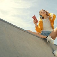 skatepark, headphones and woman on a phone listening to music for calm, gen z summer holiday on blue sky. young person with streetwear and cellphone, smartphone or 5g audio tech in urban city below - fashion stock pictures, 
