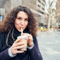 smiley woman drinking an iced coffee in the street - junk food stock pictures, royalty-free photos & images