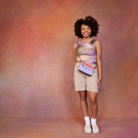 smiling afro teenage girl with sling bag standing against brown backdrop - fashion stock pictures, royalty-free photos & images