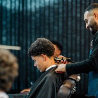 smiling barber trimming a customer's hair in a busy barber shop - hairstyle stock pictures, royalty-free photos & images