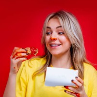 smiling blonde woman with red nose eating fried chicken wings in sauce in red studio - junk food stock pictures, royalty-free photos & images