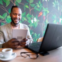 smiling businessman using a tablet and laptop over coffee in a cafe - home decoration stock pictures, royalty-free photos & images