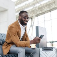 smiling businessman using smart phone in station departure lounge - travel stock pictures, royalty-free photos & images