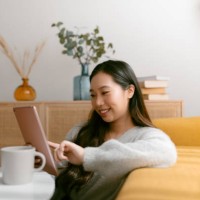 smiling chinese woman using a digital tablet while sitting on the floor in the living room at home. - home decoration stock pictures, royalty-free photos & images