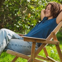 smiling curly haired woman with eyes closed resting on deck chair in garden - garden decoration photos et images de collection