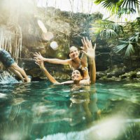 smiling daughter sitting on mothers shoulders while swimming together with family in cenote - travel stock pictures, royalty-free photos & images