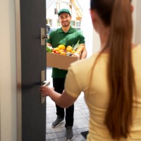 smiling deliveryman holding vegetable box while standing at entrance - food stockfoto's en -beelden
