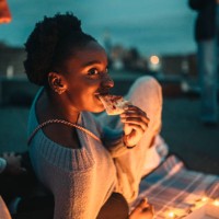 smiling female eating pizza by friend on rooftop at night - junk food stock pictures, royalty-free photos & images
