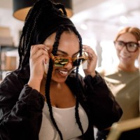 smiling female friends trying eyewear while talking at fashion store - fashion stock pictures, royalty-free photos & images