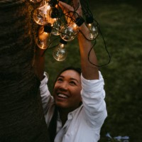 smiling female hanging lighting equipment on tree trunk in yard during dinner party - garden decoration stock pictures, royalty-free photos & images