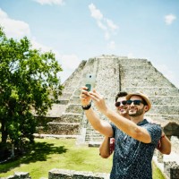 smiling gay couple taking selfie with smartphone while exploring mayapan ruins during vacation - travel stock-fotos und bilder