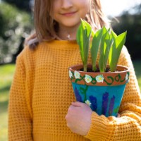 smiling girl (8-9) holding a self-painted terracotta pot filled with young tulip shoots outdoors on a sunny day in springtime. - garden decoration stock pictures, royalty-free photos & images
