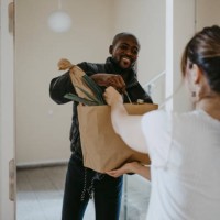 smiling man giving paper bag of groceries to woman standing at doorway - food stock pictures, royalty-free photos & images