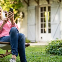 smiling mature woman using smartphone while sitting on deckchair - garden decoration photos et images de collection
