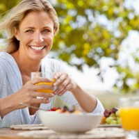 smiling mature woman with orange juice at breakfast table outdoors - food stock pictures, royalty-free photos & images