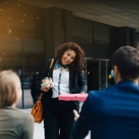 smiling mid adult businesswoman talking on mobile phone while giving food and drinks to colleagues against cafe - junk food stock pictures, royalty-free photos & images