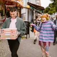 smiling non-binary person holding stack of pizza boxes while walking with friends at street in city - junk food stock pictures, royalty-free photos & images